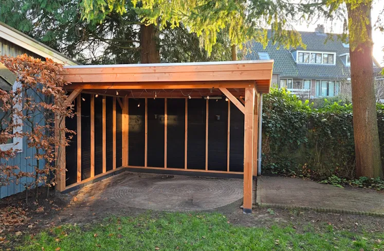 Douglas overkapping met plat dak en twee zwarte wanden van Zweeds rabat in een tuin